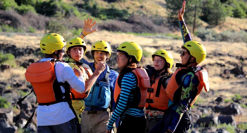 a group of students wearing life jackets and helmets stand and appear to celebrate by high-fiving 